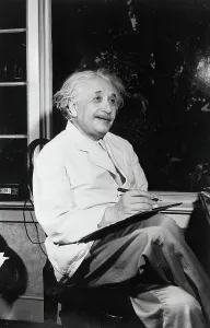 Prints of (Original Caption). Dr. Albert Einstein is shown seated inside by the window, with a smile, writing Pioneers of Science: Albert Einstein Seated at Desk Print