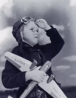 Images Dated 30th August 2005: Boy (8-10) wearing flying cap and goggles holding toy plane (B&W)