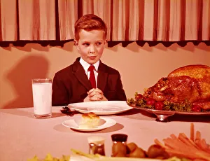 Boy sitting at table with hands folded for grace prayer, looking at roast turkey Boy sitting at table with hands folded for grace prayer, looking at roast turkey