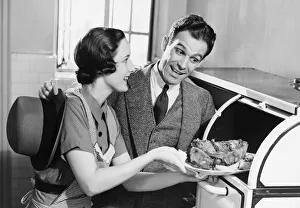 Couple in kitchen, wife taking roast from oven, (B&W) Couple in kitchen, wife taking roast from oven, (B&W)