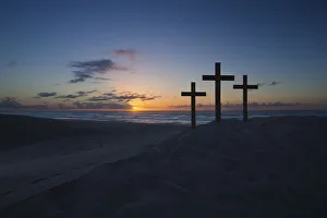 Three crosses on a sand dune next to the ocean with a cloudy sunrise Three crosses on a sand dune next to the ocean with a cloudy sunrise