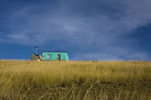 Distant view of a small traditional flat house under blue sky and surrounded by golden wavy grass , Coffee Bay Distant view of a small traditional flat house under blue sky and surrounded by golden wavy grass , Coffee Bay
