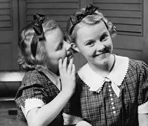 Girl (12-13) indoors whispering into ear of twin sister, (B&W) Girl (12-13) indoors whispering into ear of twin sister, (B&W)