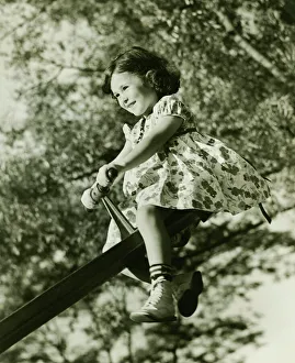 Girl (4-5) on see-saw in park, (B&W), low angle view Girl (4-5) on see-saw in park, (B&W), low angle view