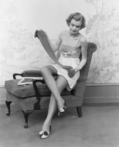 Vintage Lingerie Prints: Woman wearing lingerie, sitting on arm of chair, holding up pair of silk stockings