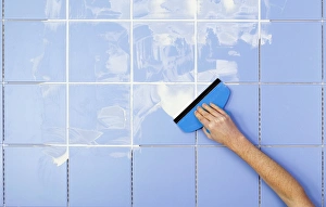 Hand spreading grout on tiles with grout spreader Hand spreading grout on tiles with grout spreader