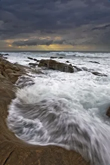 Landscape photo of ocean waves crashing onto the rocks under a stormy moody sky at Landscape photo of ocean waves crashing onto the rocks under a stormy moody sky at