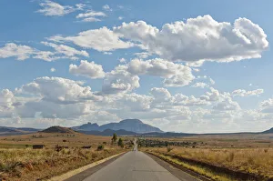 Long straight road, vast arid landscape, sky with clouds Long straight road, vast arid landscape, sky with clouds