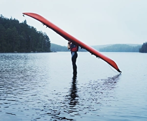 Man with kayak on head on lake surface, side view Man with kayak on head on lake surface, side view