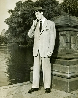 Man lighting cigarette by lake in park, (B&W) Man lighting cigarette by lake in park, (B&W)