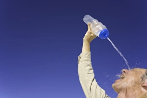 Mature man pouring water over face under clear sky, low angle view Mature man pouring water over face under clear sky, low angle view