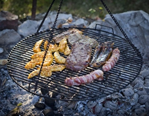 Meat and sausages being cooked on a grill hanging on chains Meat and sausages being cooked on a grill hanging on chains