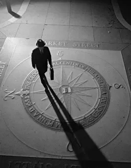 Silhouetted businessman with briefcase walking across compass in the sidewalk Silhouetted businessman with briefcase walking across compass in the sidewalk