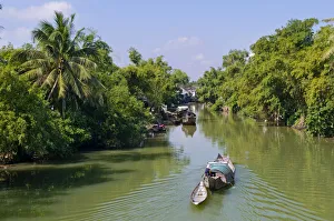 Small wooden motorboat passing through a water channel surrounded by tropical vegetation Small wooden motorboat passing through a water channel surrounded by tropical vegetation
