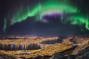 Prints of Northern lights dancing over the city of Tromso, northern Norway. Brightly illuminated streets of the Arctic Capital. Snowcapped mountains on Kvaloya Island in the background Norway Prints: Tromso Panorama with Northern Lights Print