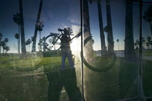 Images Dated 17th September 2005: Window reflecting palm trees and cyclist carrying bicyle