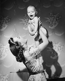 Woman lifting up baby (6-9 months) at home, (B&W) Woman lifting up baby (6-9 months) at home, (B&W)