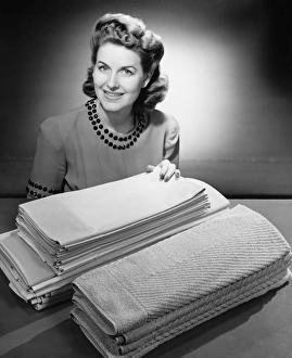 Woman sitting at pile of ironed linen and towels (B&W), portrait Woman sitting at pile of ironed linen and towels (B&W), portrait