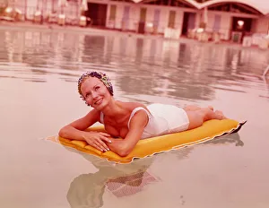 Woman in swimming pool reclining on inflatable raft, wearing bathing cap, smiling Woman in swimming pool reclining on inflatable raft, wearing bathing cap, smiling