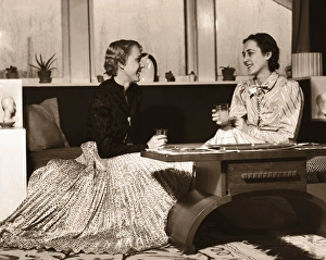 Two Women Sitting on Sofa with Drinks, Chatting Two Women Sitting on Sofa with Drinks, Chatting