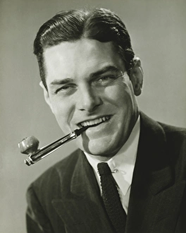 Young businessman in studio holding pipe in teeth, smiling, (B&W), portrait Young businessman in studio holding pipe in teeth, smiling, (B&W), portrait