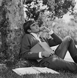 Young man leaning against tree, holding book Young man leaning against tree, holding book