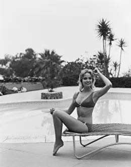 Young woman sitting on sun lounger by swimming pool, smiling, portrait Young woman sitting on sun lounger by swimming pool, smiling, portrait