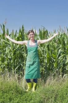 Young woman in work clothes standing with outstretched arms in front of a maize field Young woman in work clothes standing with outstretched arms in front of a maize field
