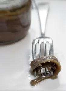Fillets of anchovies in oil in preserving jar, with single fillet on a fork credit Fillets of anchovies in oil in preserving jar, with single fillet on a fork credit
