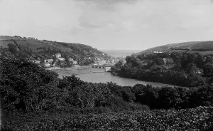 Prints of View over the trees of Trenant Wood towards Looe Bridge and beyond. The tide mill pond can be seen by the bridge and boats are moored alongside the quay. Photographer: Surgeon Captain John Campbell Looe Prints: Looe River Print, 1890s View over Trenant Wood towards Looe Bridge