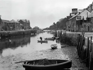 Prints of A view down river from the west end of Looe Bridge. Julians Furnishing Warehouse is on the right, and there are several men in boats on the water. Photographer: S.C. Fox Looe Prints: Print of The River Looe, Cornwall, circa 1920