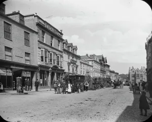 Prints of Horse buses are parked up along the busy street, including the Volunteer'. Signage for Fred J. Hosken Webb and Co. Collett and Seymour, Huddy Bros Truro Prints: Print of Truro's Boscawen Street from the west end, circa 1900