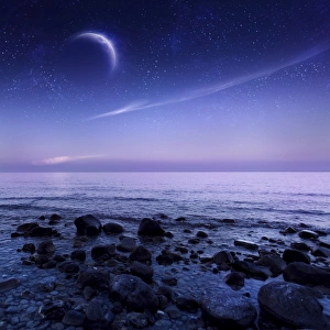 Moon rising over rocky seaside against starry sky Moon rising over rocky seaside against starry sky