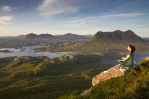 Woman meditating on Stac Pollaidh mountain with views of surrounding lochs and mountains, Assynt, Scotland, UK Woman meditating on Stac Pollaidh mountain with views of surrounding lochs and mountains, Assynt, Scotland, UK