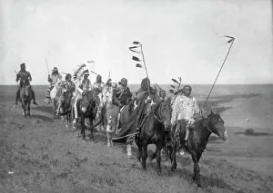 Prints of On the war path-Atsina, c1908. Small band of Atsina men on horseback, some carrying staffs with feathers, one wearing a war bonnet Edward Curtis Prints: On the War Path-Atsina, c1908 Print: Atsina Men on Horseback