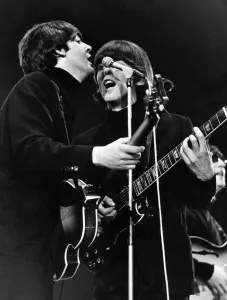 Paul McCartney and George Harrison share a microphone on stage Paul McCartney and George Harrison share a microphone on stage
