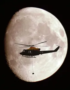 A Griffin Helicopter, with an underslung load, shown in silhouette against a full moon A Griffin Helicopter, with an underslung load, shown in silhouette against a full moon