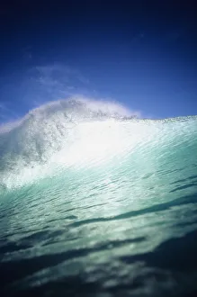 Closeup angle of green wave with backlit crest, bright blue sky Closeup angle of green wave with backlit crest, bright blue sky