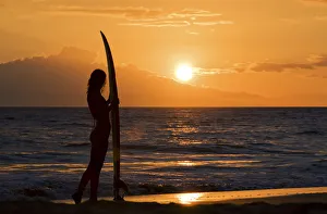 Hawaii, Female Surfer On Beach Silhouetted Against Orange Sunset Over Ocean Hawaii, Female Surfer On Beach Silhouetted Against Orange Sunset Over Ocean