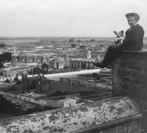 Historic image in black and white of a boy and his Chihuahua dog sitting high up on a wall overlooking the city of San Historic image in black and white of a boy and his Chihuahua dog sitting high up on a wall overlooking the city of San