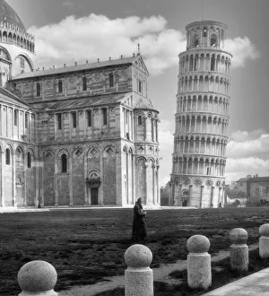 Historic image in black and white of the Leaning Tower of Pisa, Pisa Cathedral and a monk standing in the foreground Historic image in black and white of the Leaning Tower of Pisa, Pisa Cathedral and a monk standing in the foreground