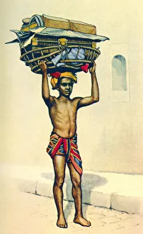An Indian porter carrying a large basket of luggage on his head, India, from a contemporary print, c.1935; Artwork An Indian porter carrying a large basket of luggage on his head, India, from a contemporary print, c.1935; Artwork