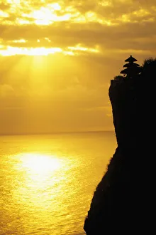 Indonesia, Bali, Uluwatu Temple Silhouetted In Distance Along Cliff, Golden Sunset Indonesia, Bali, Uluwatu Temple Silhouetted In Distance Along Cliff, Golden Sunset