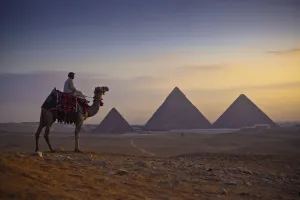 A Lone Camel And Rider Stand In Front Of The Setting Sun With The Great Pyramids Behind A Lone Camel And Rider Stand In Front Of The Setting Sun With The Great Pyramids Behind