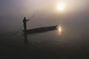 A Man Pushes His Dugout Canoe Along The Rapti River Near Sauraha And Chitwan National Park At Dawn; Nepal A Man Pushes His Dugout Canoe Along The Rapti River Near Sauraha And Chitwan National Park At Dawn; Nepal