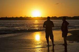 Two Men Stand In The Tide Water On A Beach At Sunset; Caloundra, Queensland, Australia Two Men Stand In The Tide Water On A Beach At Sunset; Caloundra, Queensland, Australia