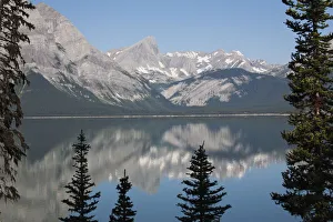 Mountain lake reflecting mountain range with snow and blue sky framed by trees in kananaskis provincial park Mountain lake reflecting mountain range with snow and blue sky framed by trees in kananaskis provincial park