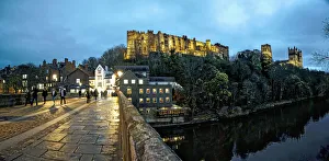 Pedestrians Walking On A Walkway Over A River At Dusk With Durham Cathedral And Castle On A Hilltop; Durham, England Pedestrians Walking On A Walkway Over A River At Dusk With Durham Cathedral And Castle On A Hilltop; Durham, England