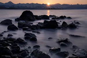 Silhouette of rock formations and misty water with sun setting behind mountains, USA Silhouette of rock formations and misty water with sun setting behind mountains, USA
