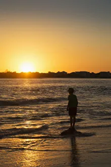 Silhouette Of A Young Boy Standing At The Waters Edge At Sunset; Caloundra, Queensland Silhouette Of A Young Boy Standing At The Waters Edge At Sunset; Caloundra, Queensland
